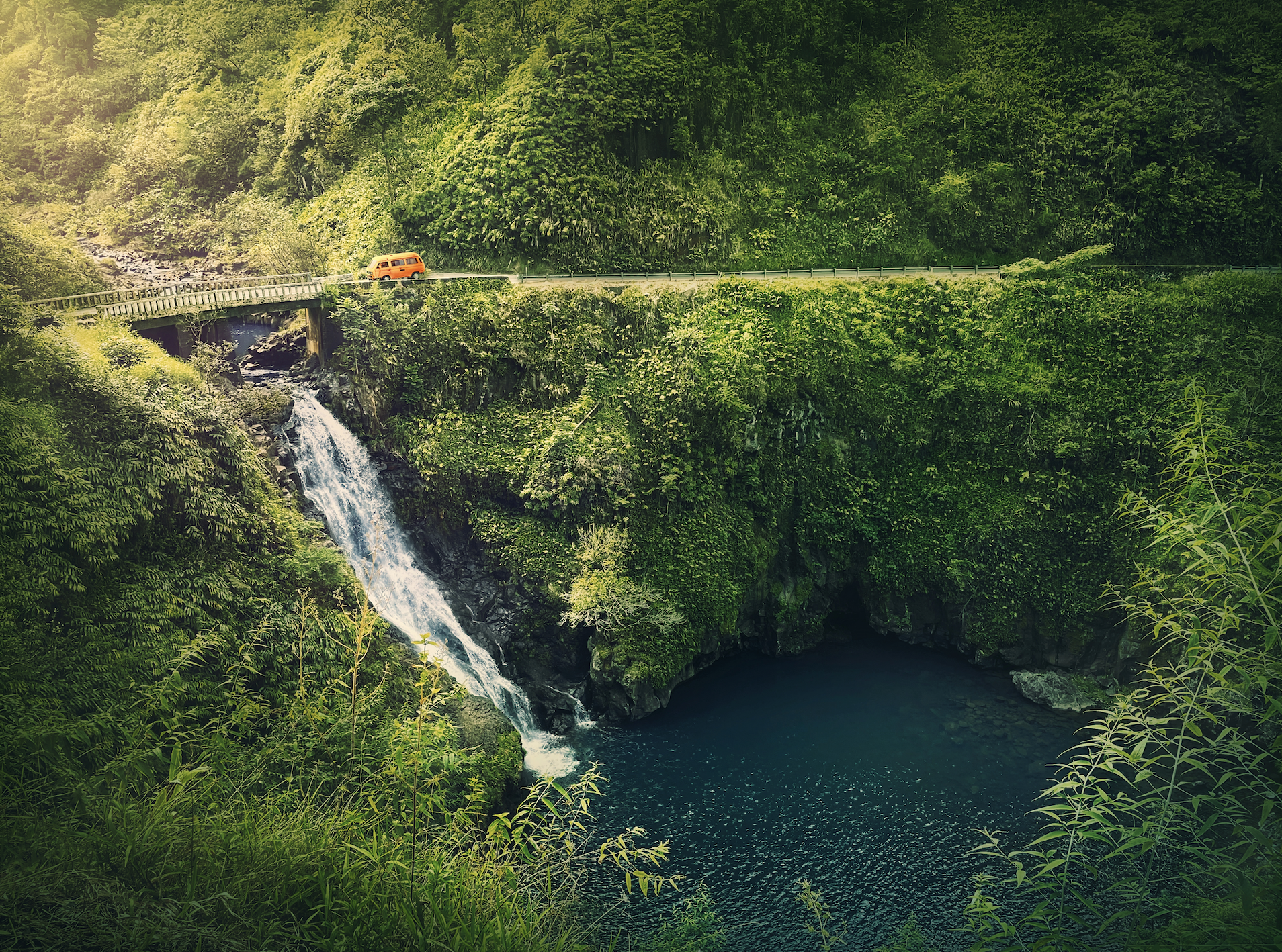view of Makapipi Falls. waterfall under bridge as orange van drives along road