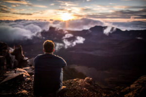 A man sitting on Haleakala Volcano watching the sun rise on a maui private tour